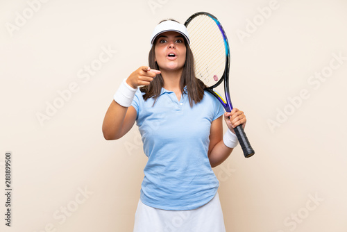 Young woman playing tennis over isolated background surprised and pointing front