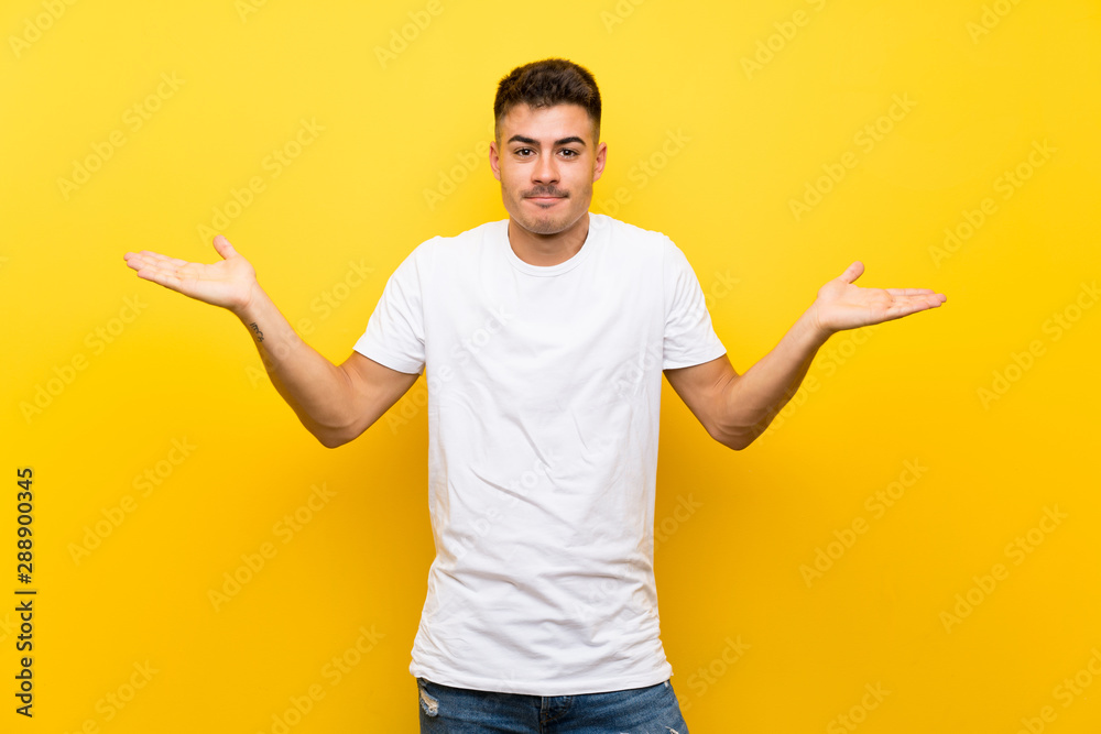Young handsome man over isolated yellow background having doubts while raising hands Young handsome man over isolated yellow background having doubts while raising hands