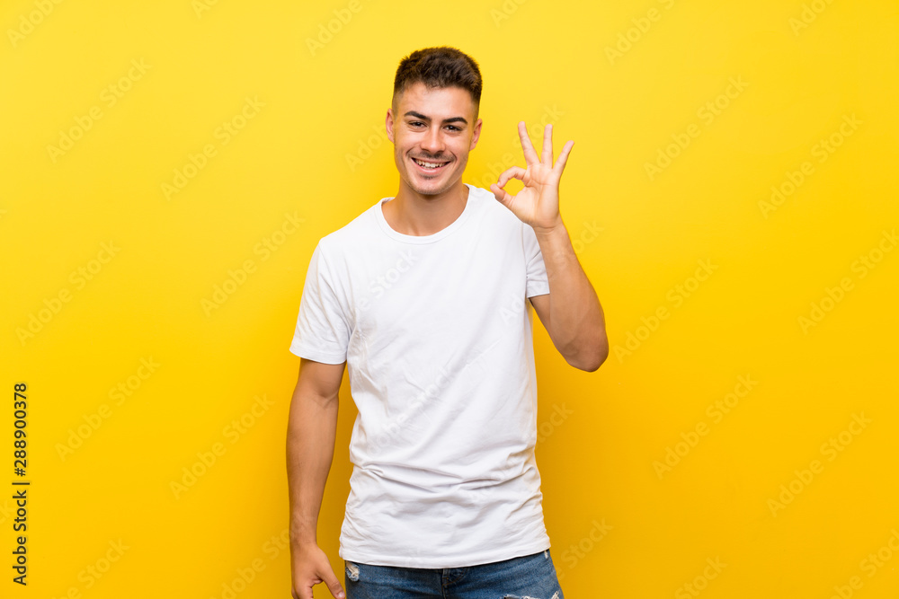 Young handsome man over isolated yellow background showing ok sign with fingers Young handsome man over isolated yellow background showing ok sign with fingers