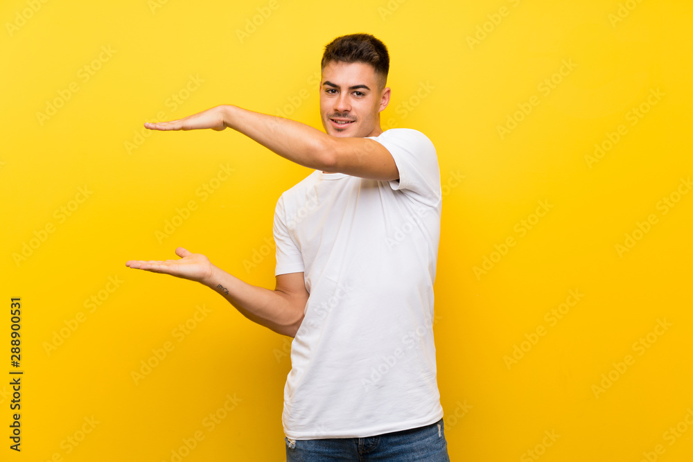 Young handsome man over isolated yellow background holding copyspace to insert an ad Young handsome man over isolated yellow background holding copyspace to insert an ad