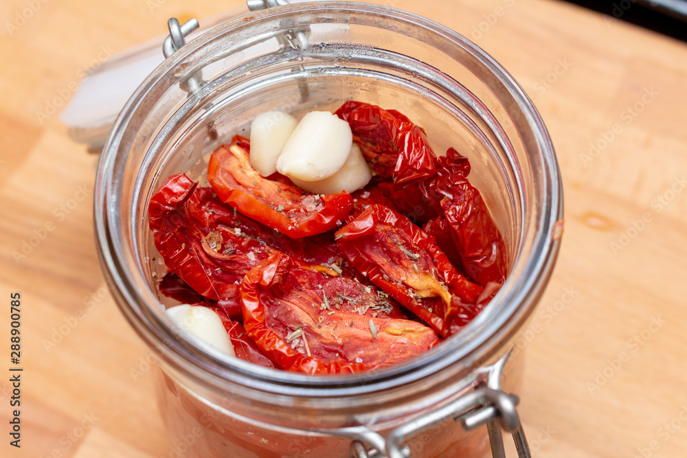 Homemade dried red  tomatoes slices with basil oregano spices in a glass jar. Traditional Italian Mediterranean kitchen cuisine.