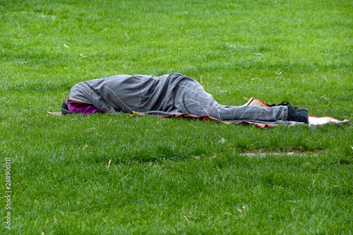 Homeless man wrapped in blanket sleeping on green grass