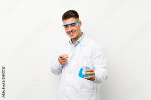 Young scientific holding laboratory flask over isolated background points finger at you