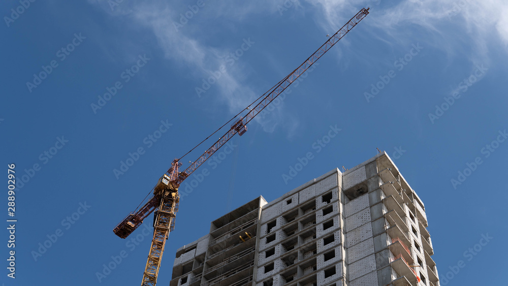 Modern building under construction with crane. From below of constructing building with high crane under clear sky Modern building under construction with crane. From below of constructing building with high crane under clear sky
