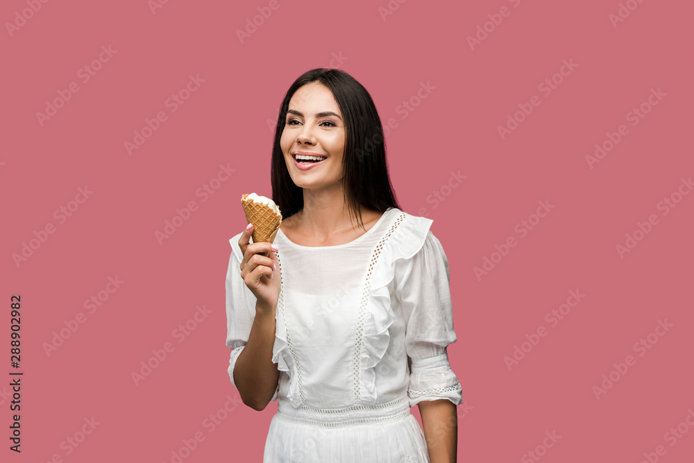 cheerful young woman in dress holding tasty ice cream cone isolated on pink