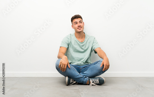 Young handsome man sitting on the floor laughing and looking up