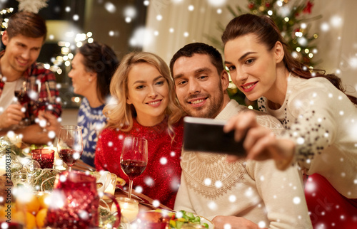 holidays and celebration concept - happy friends having christmas dinner at home and taking selfie by smartphone over snow