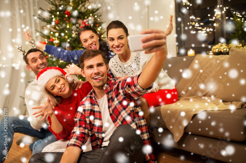 celebration and holidays concept - happy friends with glasses celebrating christmas at home party and taking selfie by smartphone over snow