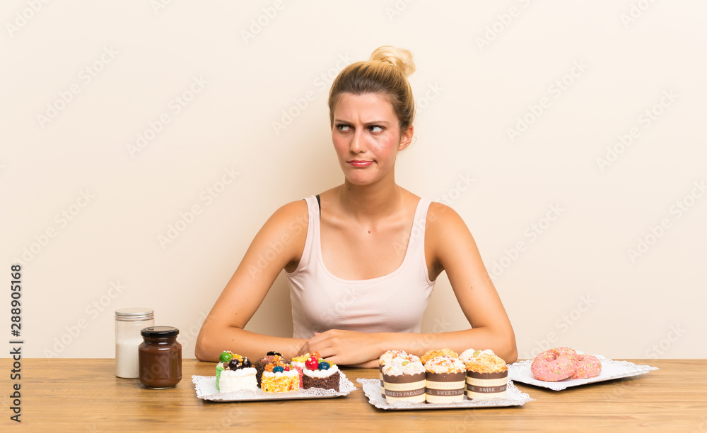 Young woman with lots of different mini cakes in a table standing and looking to the side Young woman with lots of different mini cakes in a table standing and looking to the side