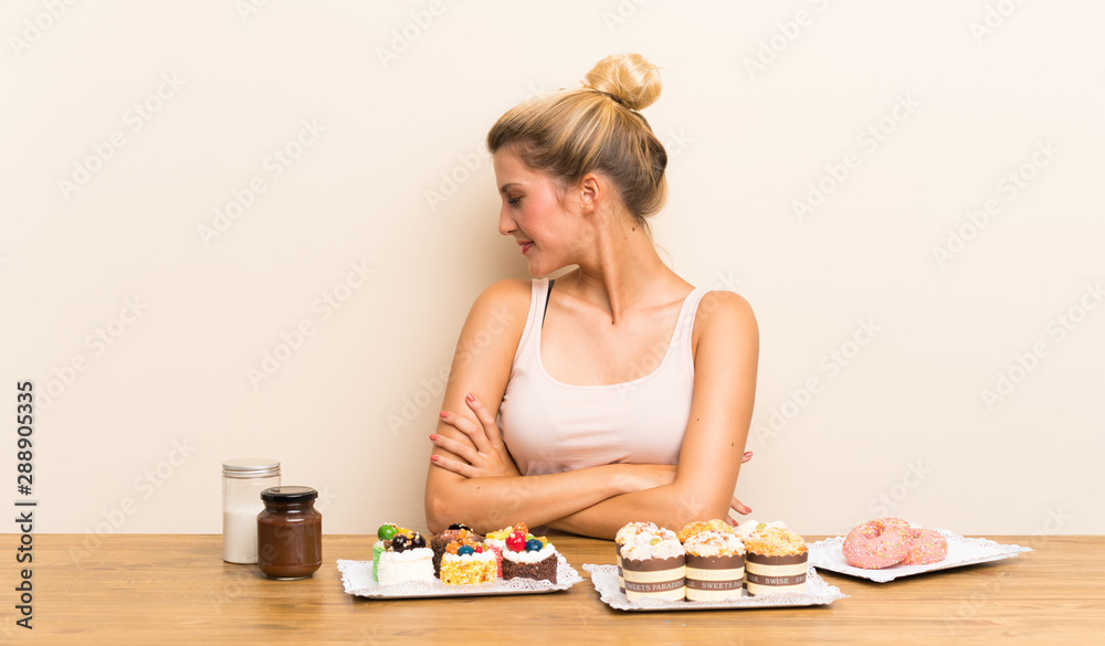 Young woman with lots of different mini cakes in a table laughing Young woman with lots of different mini cakes in a table laughing