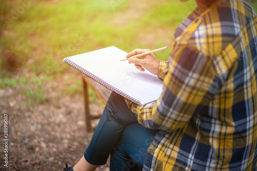 Woman in shirt sit and writing on an blank notebook with a pen. 