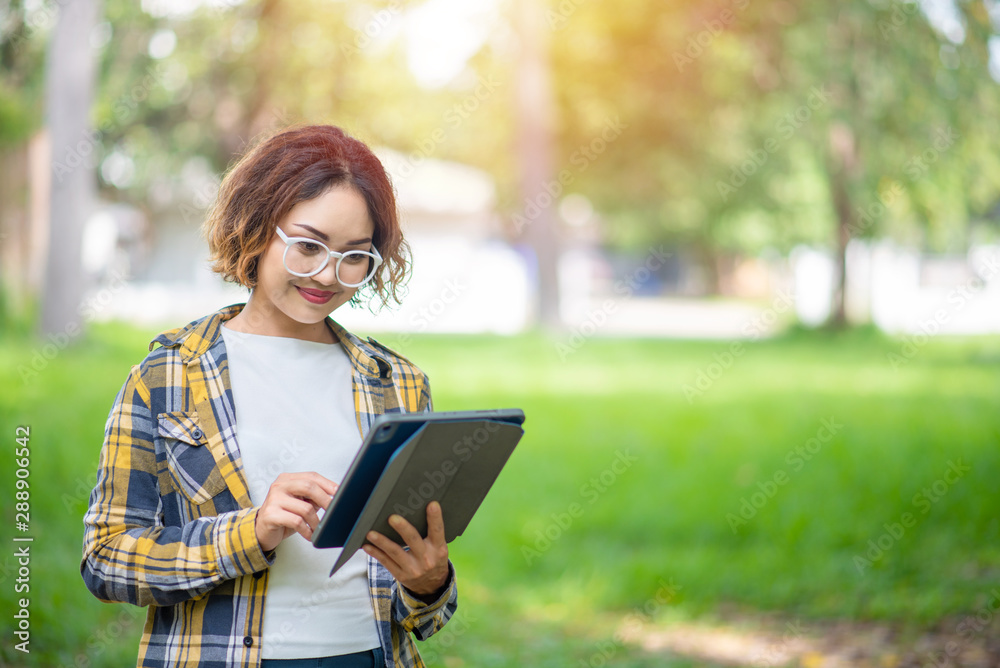 Fototapeta premium Happy woman using and looking at her digital tablet outdoors, Woman in shirt using digital tablet outdoors