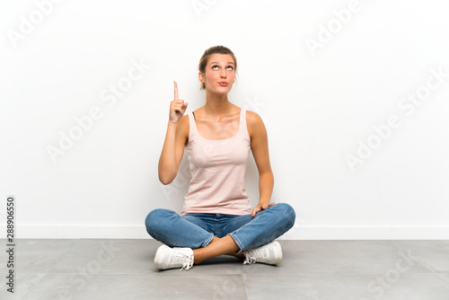 Young blonde woman sitting on the floor pointing with the index finger a great idea