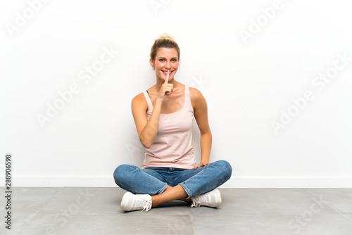 Young blonde woman sitting on the floor doing silence gesture