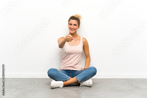 Young blonde woman sitting on the floor handshaking after good deal