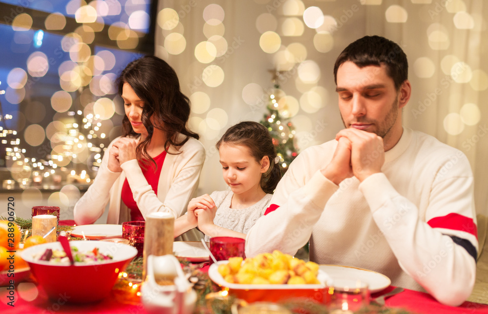 holidays, family and celebration concept - happy mother, father and little daughter having christmas dinner and praying before meal at home