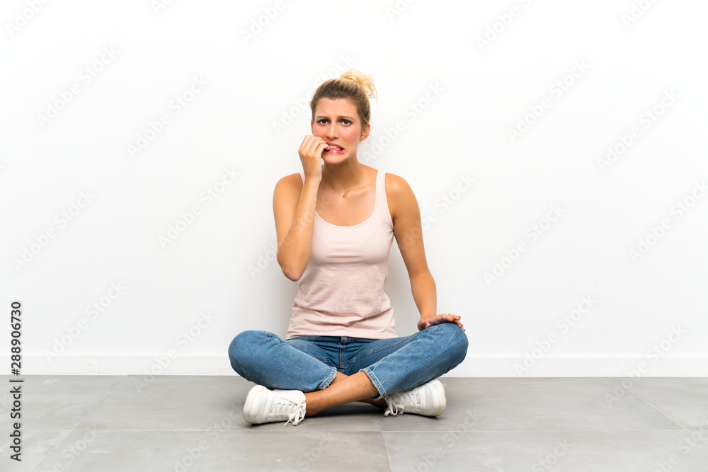 Young blonde woman sitting on the floor nervous and scared