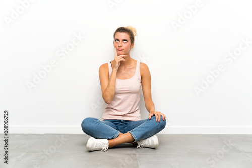 Young blonde woman sitting on the floor thinking an idea