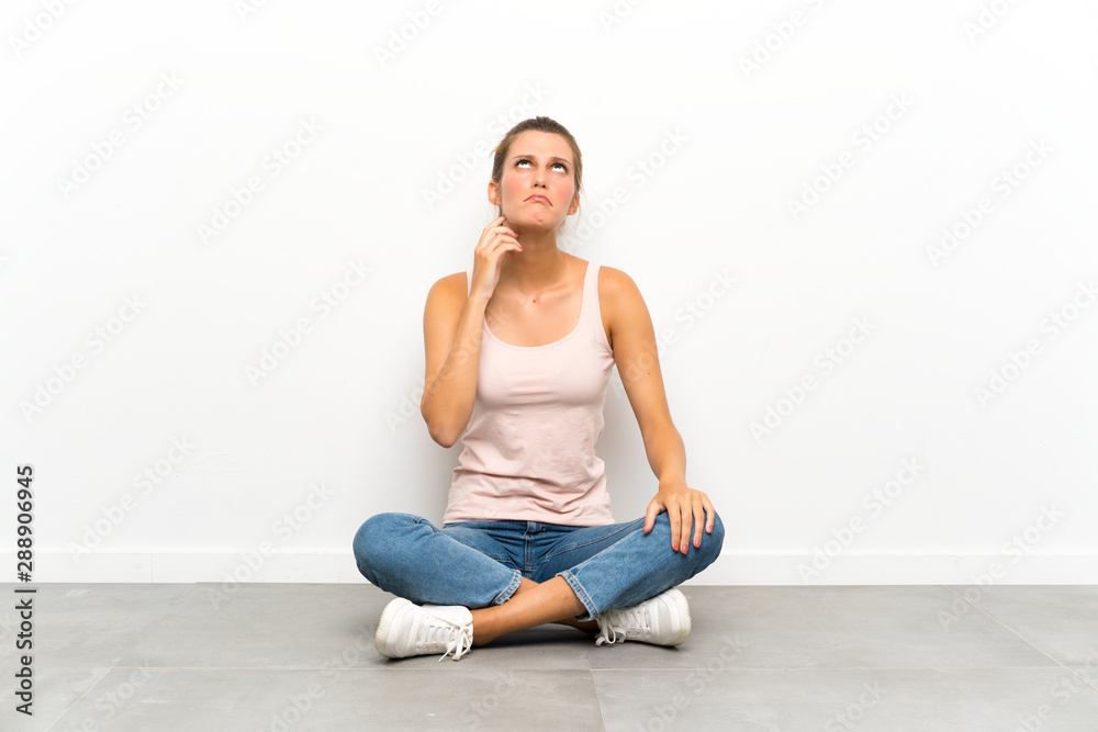 Young blonde woman sitting on the floor thinking an idea Young blonde woman sitting on the floor thinking an idea