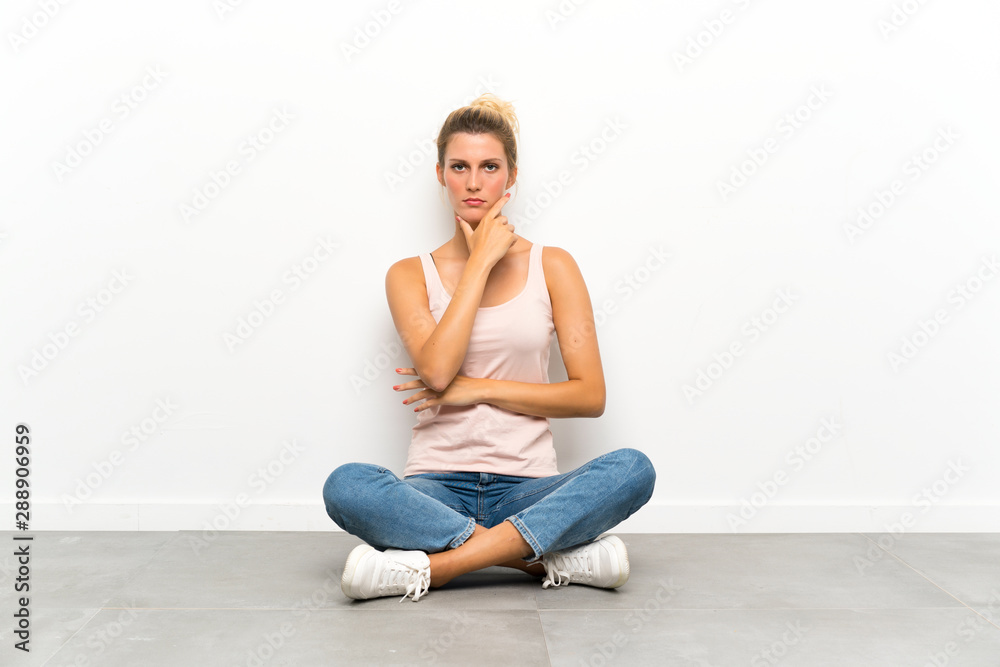 Young blonde woman sitting on the floor thinking an idea Young blonde woman sitting on the floor thinking an idea