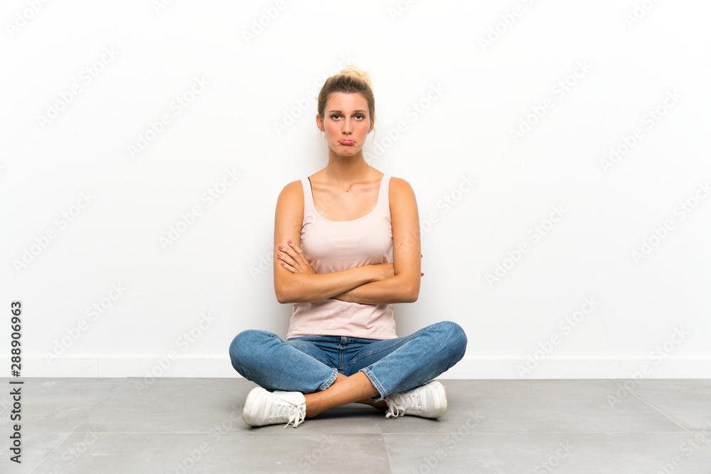 Young blonde woman sitting on the floor sad Young blonde woman sitting on the floor sad