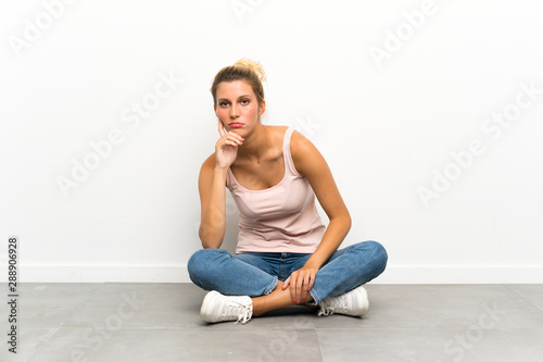 Young blonde woman sitting on the floor unhappy and frustrated