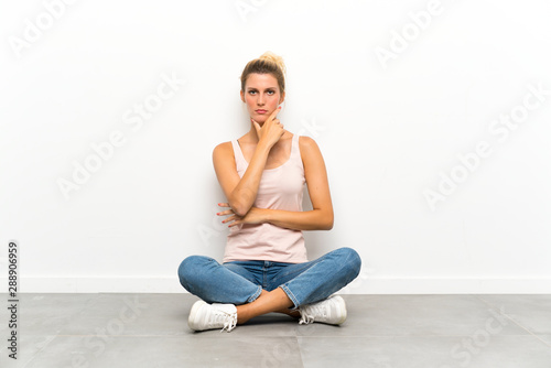 Young blonde woman sitting on the floor thinking an idea