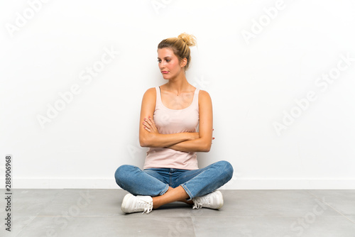 Young blonde woman sitting on the floor thinking an idea