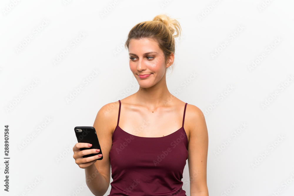 Young blonde woman using mobile phone standing and looking to the side Young blonde woman using mobile phone standing and looking to the side