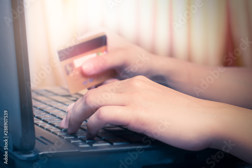 A woman holds a credit card while shopping online on a laptop