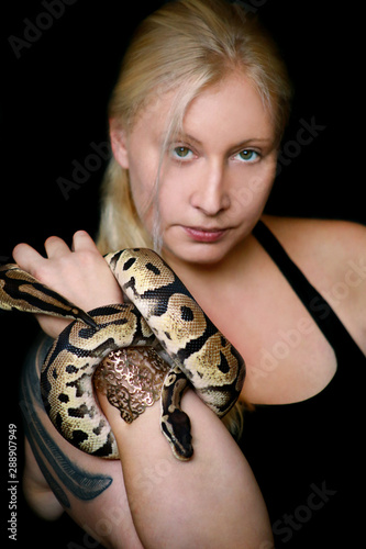 Portrait of girl with Royal Python snake. Woman holds snake in hands with beauty jewelry and posing in front of camera. Exotic tropical cold-blooded reptile, Ball Python (Python regius) species snake.