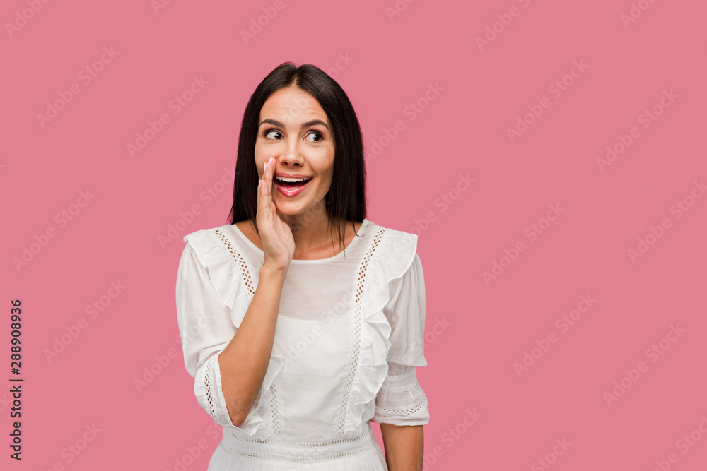cheerful woman touching face while gossiping isolated on pink cheerful woman touching face while gossiping isolated on pink
