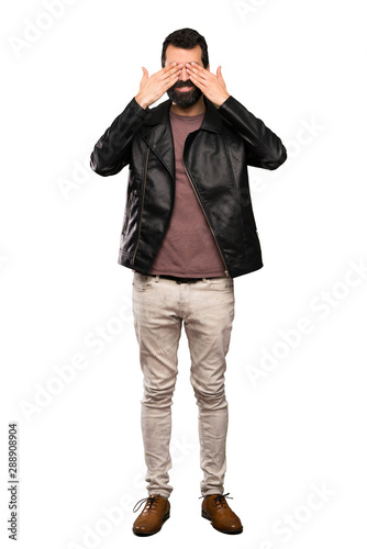 Handsome man with beard covering eyes by hands over isolated white background