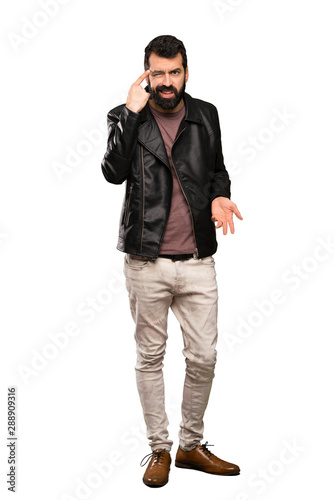 Handsome man with beard making the gesture of madness putting finger on the head over isolated white background