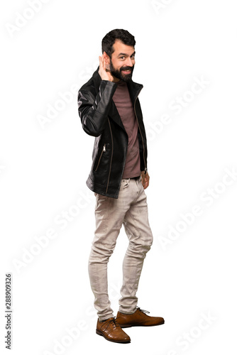 Handsome man with beard listening to something by putting hand on the ear over isolated white background