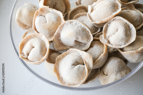 Traditional meat dumplings in a transparent plate after freezing for quick cooking. The national dish of Russian cuisine on a white background.