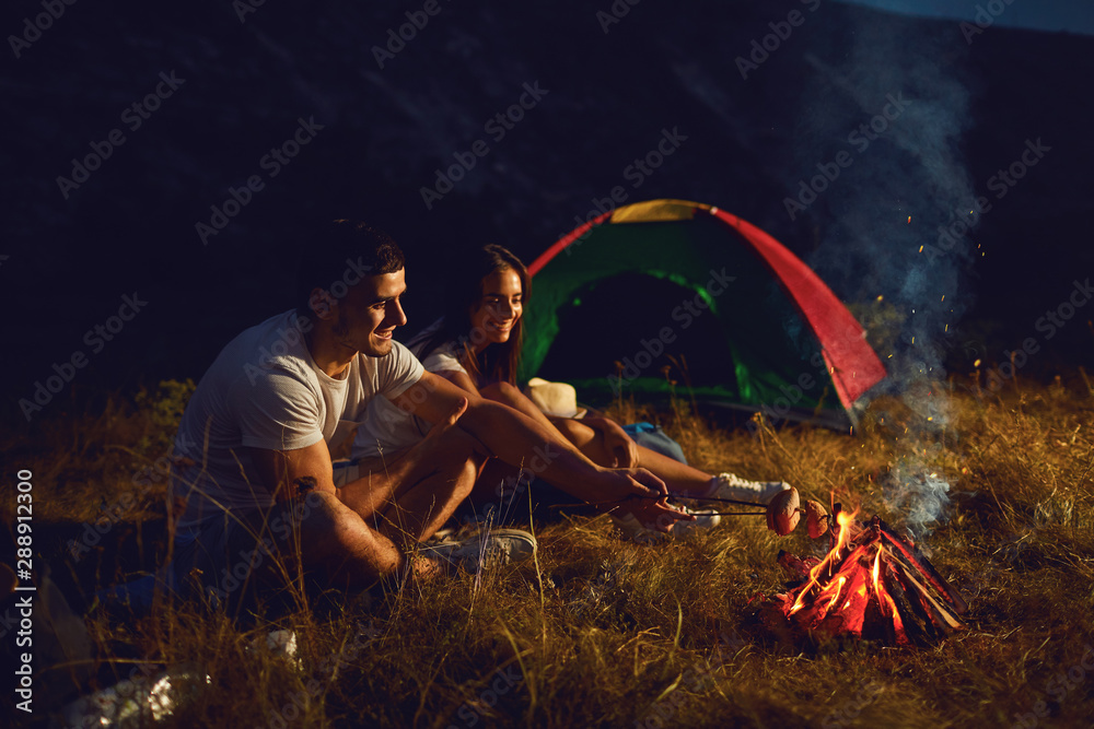 Young couple tourists on camping night cook bread by campfire