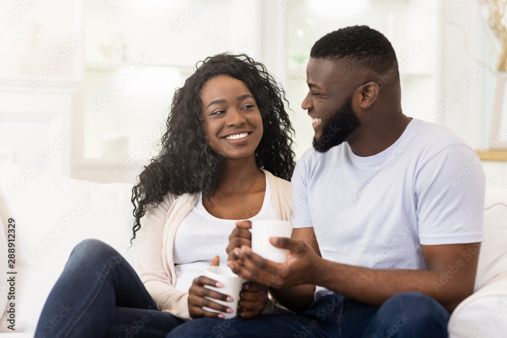 Loving millennial couple relaxing with cup of coffee at home