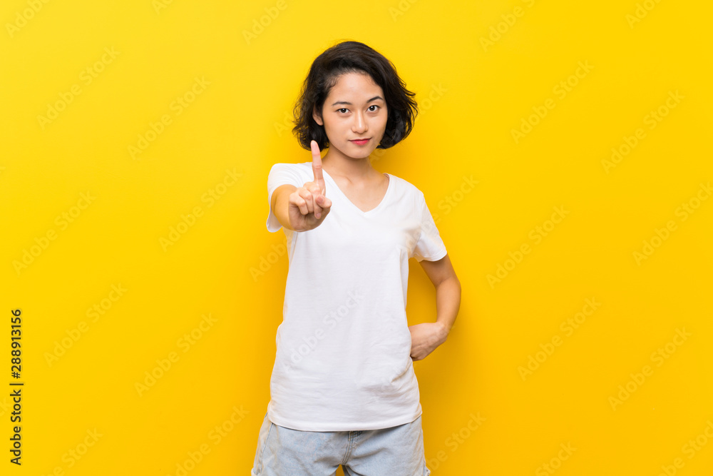 Asian young woman over isolated yellow wall showing and lifting a finger Asian young woman over isolated yellow wall showing and lifting a finger