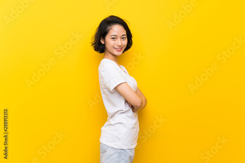 Asian young woman over isolated yellow wall with arms crossed and looking forward