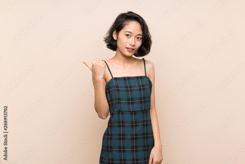 Asian young woman over isolated yellow wall pointing to the side to present a product Asian young woman over isolated yellow wall pointing to the side to present a product