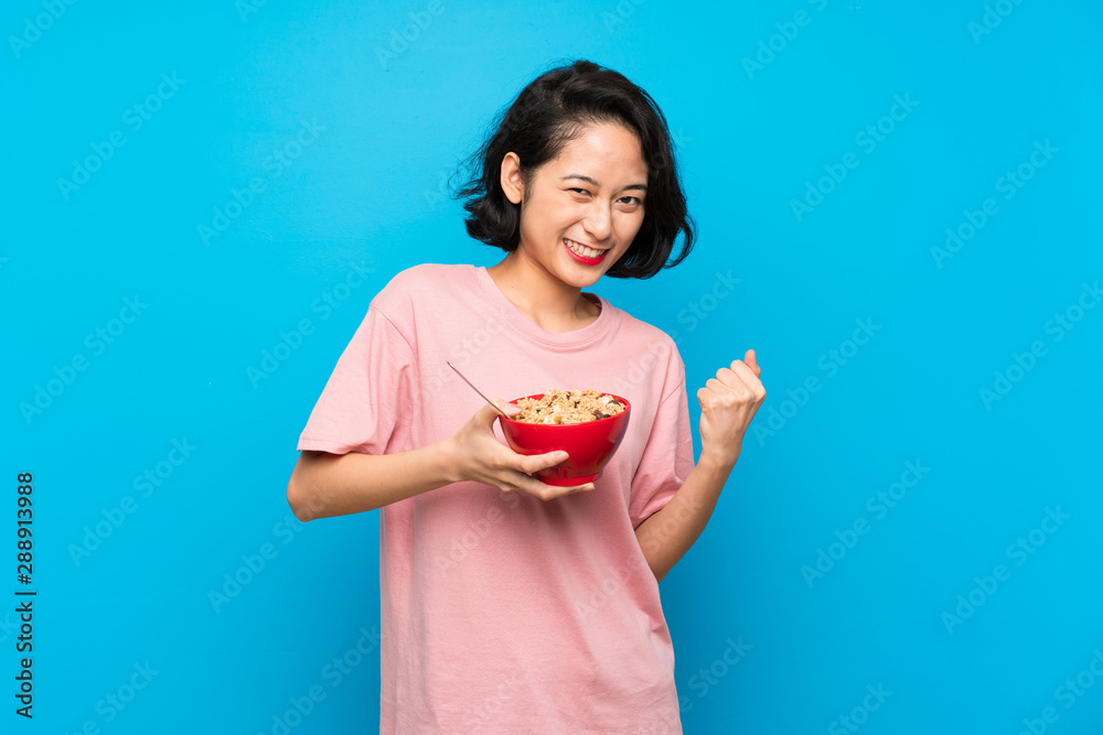 Asian young woman holding a bowl of cereals celebrating a victory Asian young woman holding a bowl of cereals celebrating a victory