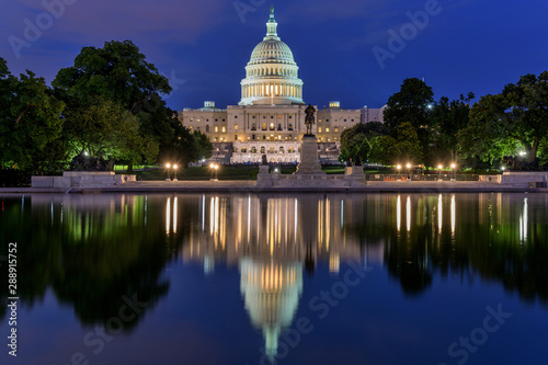 The Capitol in Reflecting Pool - A dusk view of west side of U.S. Capitol Building, with a crowd gathering around a concert at front, Washington, D.C., USA. No recognizable trademark or person.