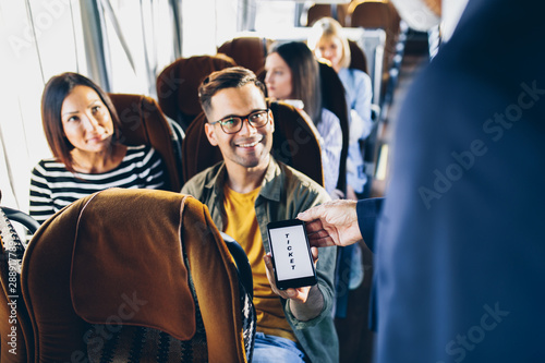 Young male traveler showing  e-ticket on mobile phone screen to a bus driver.