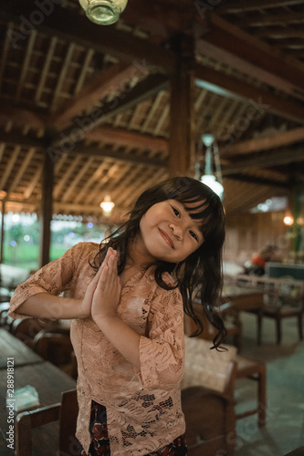 Asian little girl greets in traditional way with both hands, wearing kebaya traditional clothes from indonesia © Odua Images