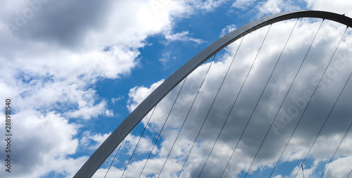 Abstract image of the Gateshead Millennium Bridge showing the arch of the bridge against a cloudy blue sky with cables heading towards the bottom of the image. photo