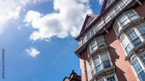 Fotografie Dynamic angle of a multi-storey building that has ornate old style sash windows with red/pink brick work and apex roofline cutting into the summer sky