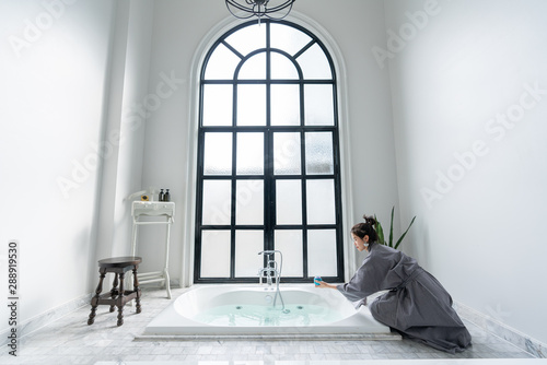 Women in bathrobe while carryin bathbomb in nice design jacuzzi bathtub with high transparant window in natural light setting scene / cozy interior concept / asian women / treatment spa photo