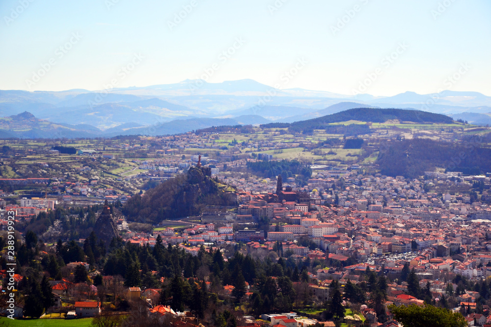 Aiguilhe, France - March 30th 2019 : view of the city Le Puy-en-Velay, built in a volcanic landscape. You can see the statue of the Virgin, the Church Saint Michel d'Aiguilhe and the cathedral.