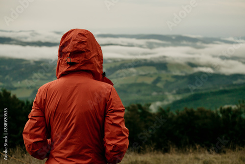 Back view of girl tourist in orange jacket looking at beautiful scenery of mountains